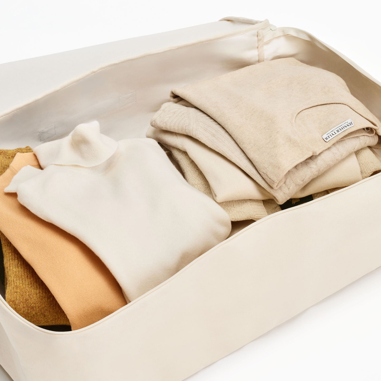 A storage bag filled with folded beige, cream, and brown sweaters.