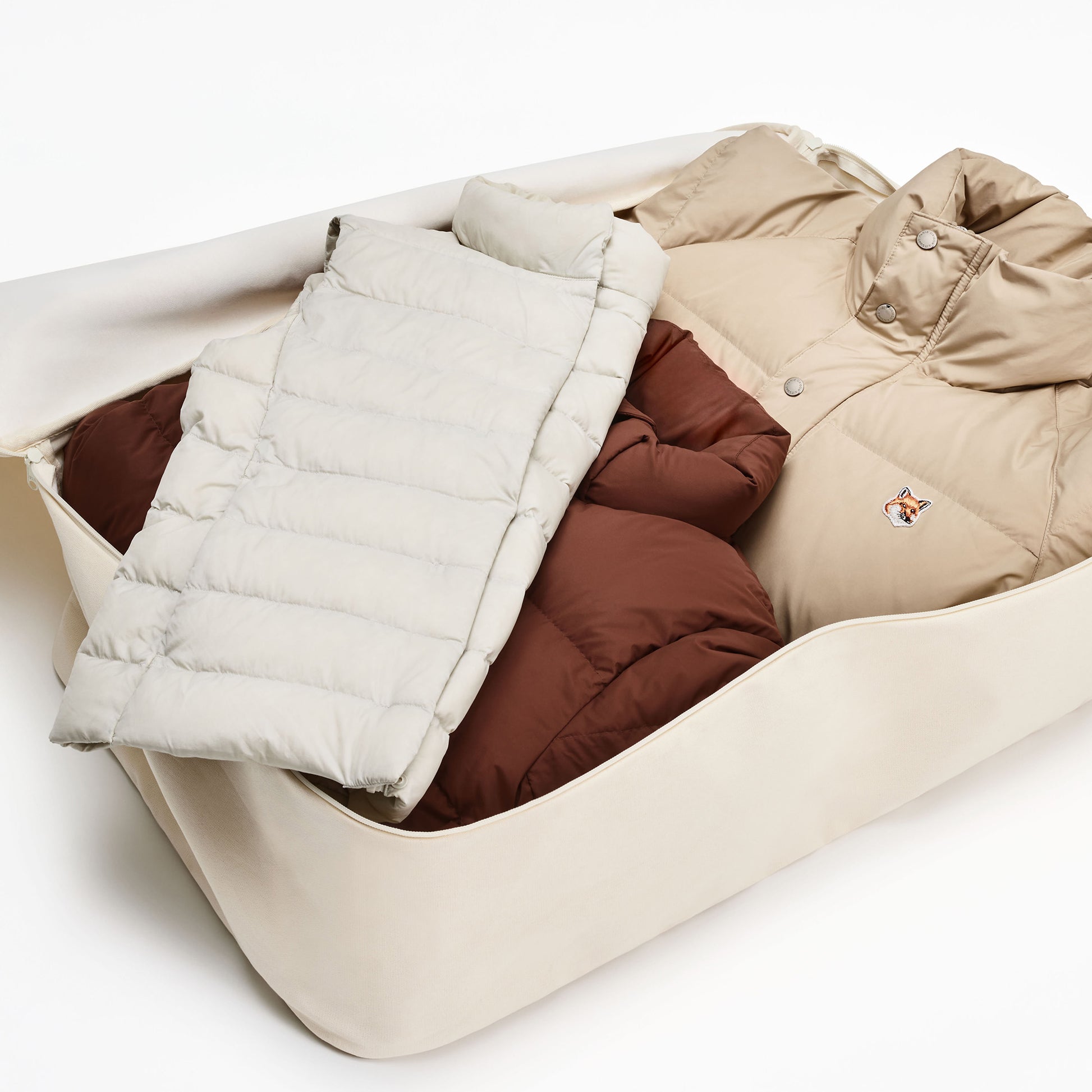 A tan puffer jacket and a folded white padded item are placed inside a beige storage bag.